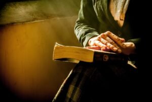 Morning Prayer For The Heartbroken: Individual praying beside bed in early morning light seeking emotional healing.”